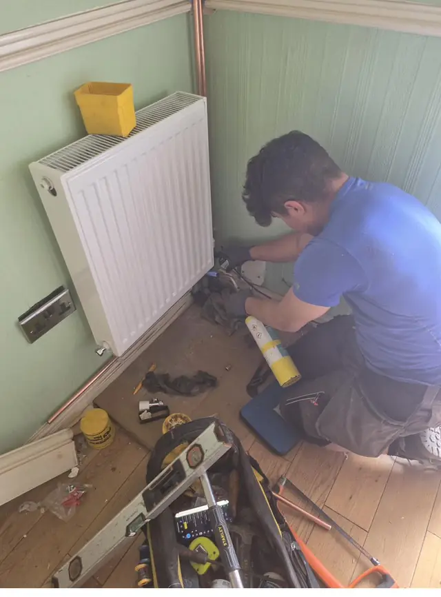 Heating engineer fitting radiator during full heating system installation